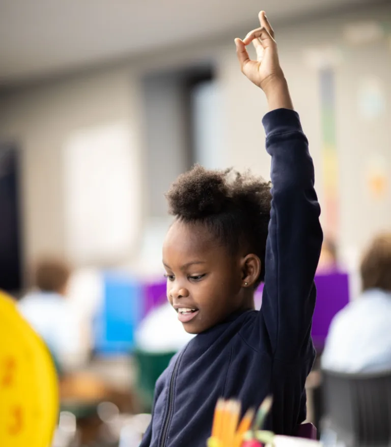 A child raising her hand in a classroom