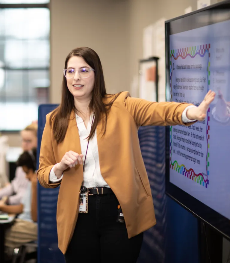 A woman teaching a class next to a television screen