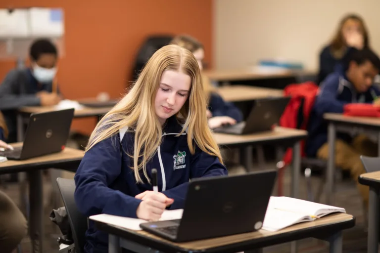 A student taking notes at her desk with her notebook and laptop